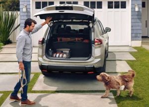 A person and their dog standing behind a 2024 Nissan Rogue parked in their driveway with its rear liftgate open near Indianapolis, Indiana