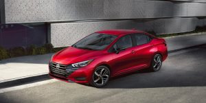 2025 Nissan Versa in red parked along a modern city sidewalk, highlighting its sleek compact sedan design.