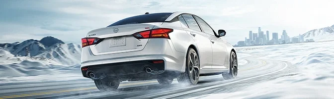 White Nissan Altima driving on a snowy road