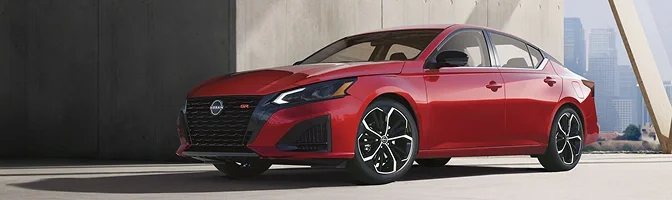 Red Nissan Altima parked in front of city buildings