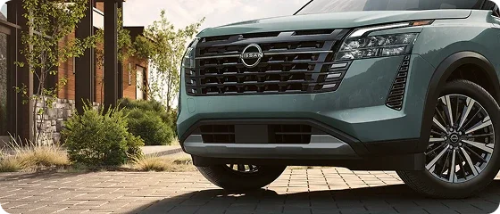 Front grille and headlight of the 2026 Nissan Pathfinder Platinum 4WD in teal, parked on a paved driveway