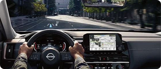 Driver's view through the windshield of the 2026 Nissan Pathfinder Platinum 4WD showing the head-up display and 12.3-inch screens on a city street