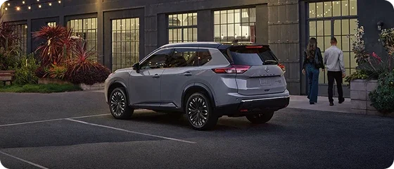 2026 Nissan Rogue Platinum AWD in gray parked outside a lit building at dusk, rear three-quarter view