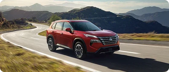 2026 Nissan Rogue Platinum AWD in red driving on a winding mountain road, front three-quarter view