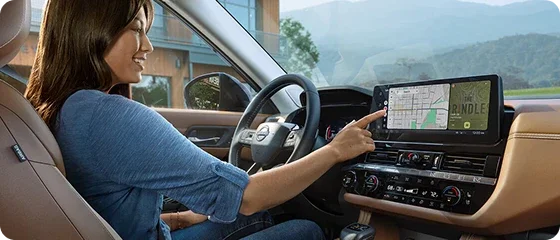 Driver reaching for the 12.3-inch NissanConnect touchscreen in the 2026 Nissan Pathfinder Platinum 4WD, with navigation on screen