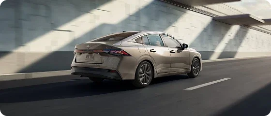 2026 Nissan Sentra SV in champagne driving alongside a concrete wall, rear three-quarter view
