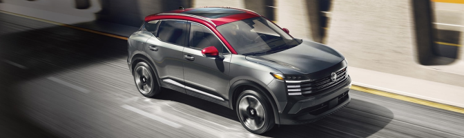 Gray Nissan SUV with a red roof driving along a city street