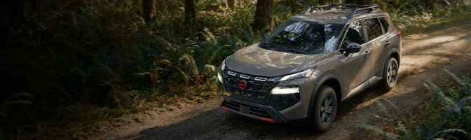 Gray Nissan SUV driving down a dirt road through a forest