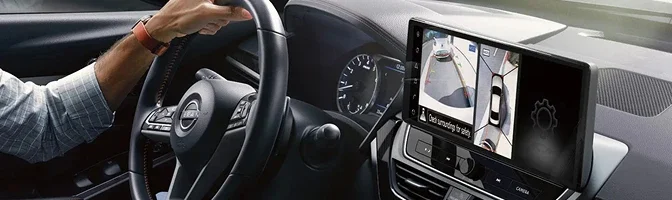 Driver at the wheel of a Nissan Altima with the around-view camera display on the center screen