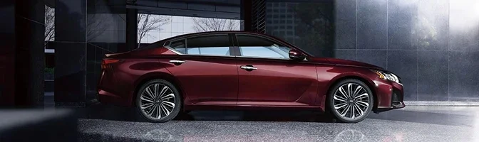 Side profile of a deep red 2026 Nissan Altima outside a glass-walled building