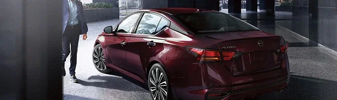 Rear three-quarter view of a deep red 2026 Nissan Altima as a driver walks up to it
