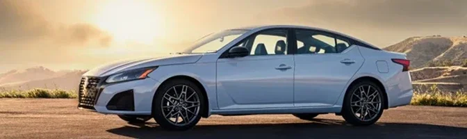 Side profile of a white 2026 Nissan Altima parked on a ridge at sunset