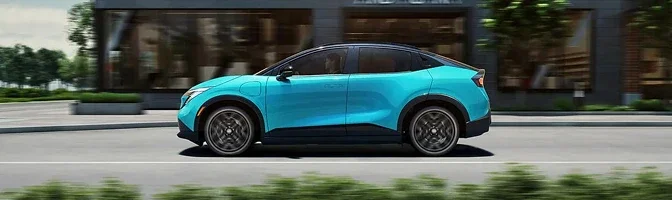 Side profile of a turquoise 2026 Nissan LEAF driving past a row of storefronts