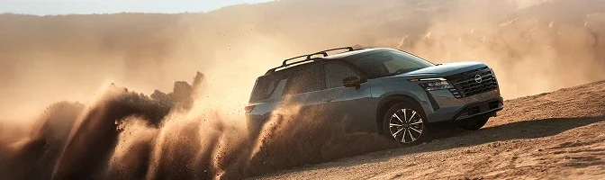 Blue-grey 2026 Nissan Pathfinder throwing up dust on a desert trail at sunset