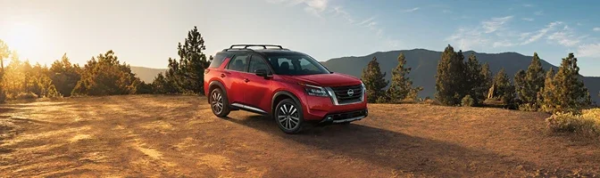 Red 2026 Nissan Pathfinder parked on a pine ridge at sunrise