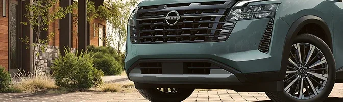 Close-up of the grille and front wheel on a green 2026 Nissan Pathfinder in a driveway