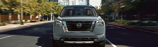 Grey 2026 Nissan Pathfinder driving toward the camera on a tree-lined city street