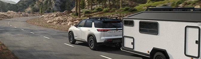 White 2026 Nissan Pathfinder towing a travel trailer along a mountain highway