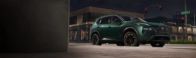 Dark green 2026 Nissan Rogue parked on a city street at night