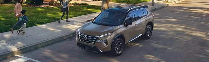 Bronze 2026 Nissan Rogue parked on a residential street as a family walks past