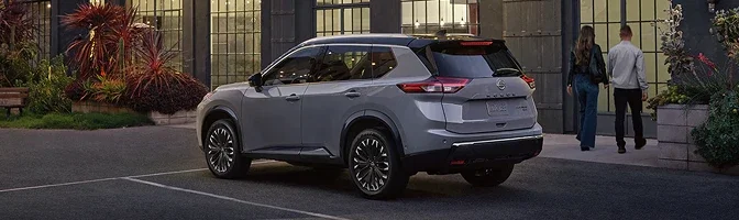 Grey 2026 Nissan Rogue parked outside a lit building as two people walk in