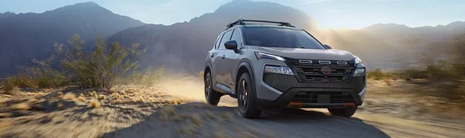 Grey Nissan Rogue Rock Creek driving a dusty desert track at sunset