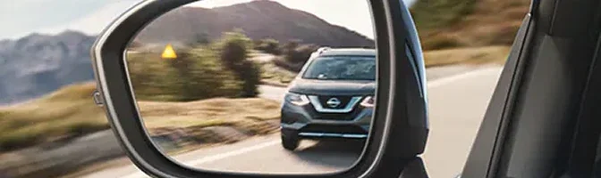 Side mirror of a Rogue showing the blind-spot warning icon and a car alongside