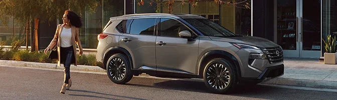 Silver 2026 Nissan Rogue parked at a storefront as a woman walks toward it