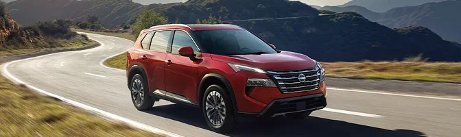 Red 2026 Nissan Rogue driving a curving road through the hills
