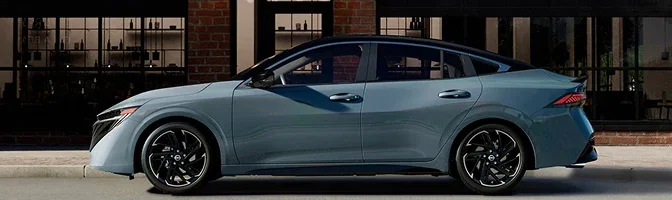 Side profile of a blue-grey 2026 Nissan Sentra parked outside a brick storefront