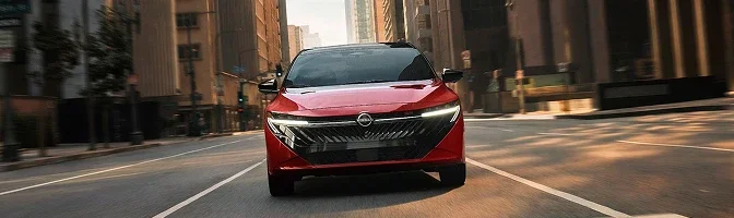 Front view of a red 2026 Nissan Sentra driving down a city street at sunrise
